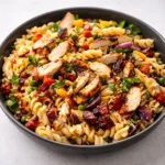A vibrant bowl of BBQ Chicken Pasta Salad on a wooden table.