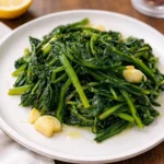 Sautéed Dandelion Greens with Garlic on a white plate with lemon.